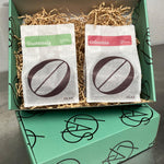 Two coffee bags labeled 'Guatemala' and 'Colombia' in a green box with decorative elements.