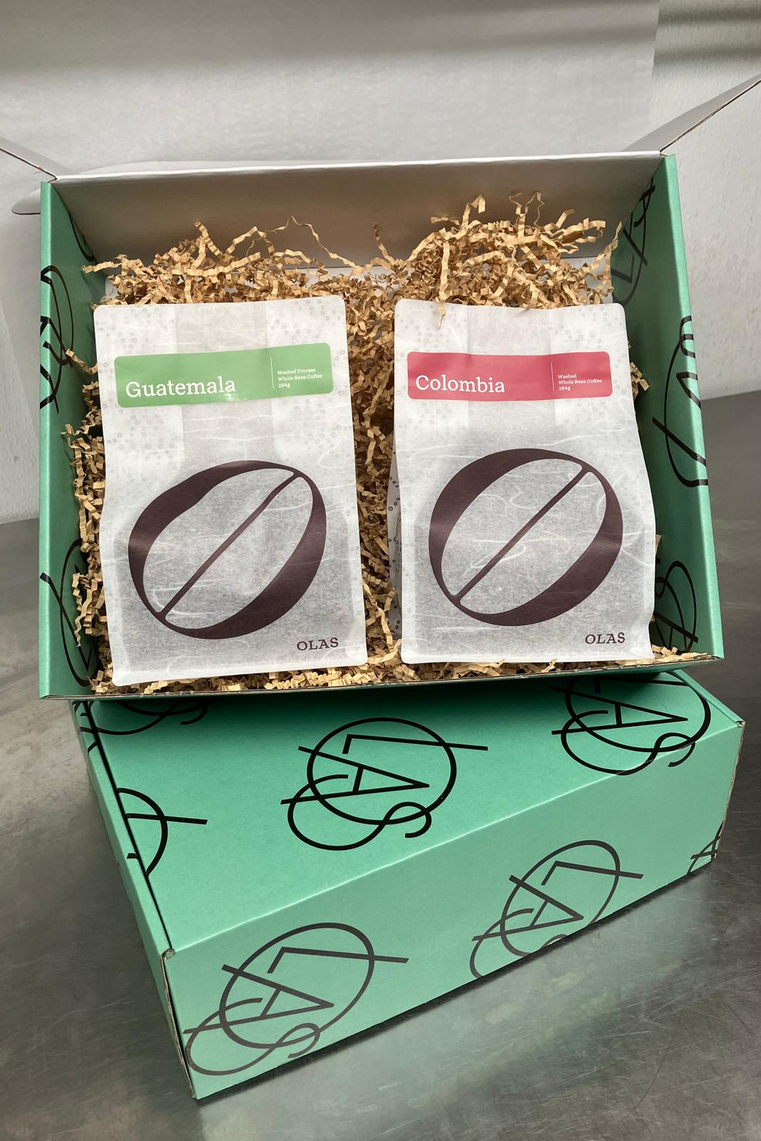 Two coffee bags labeled 'Guatemala' and 'Colombia' in a green box with decorative elements.